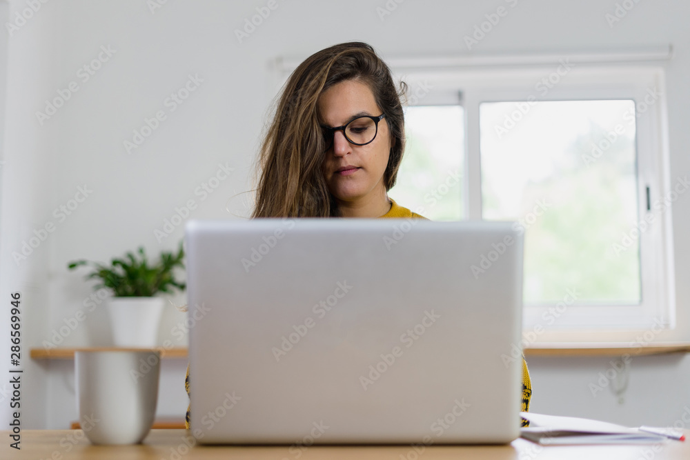 Young Girl with glasses view from the front working on her laptop computer with a mug on her side. Young Girl with glasses view from the front working on her laptop computer with a mug on her side.