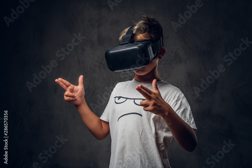 Small trendy kid is playing new shooting videogame using special virtual reality goggles.