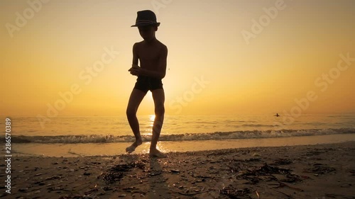 Boy with hat throwing skipping stone in sea sunset, SLOW MOTION