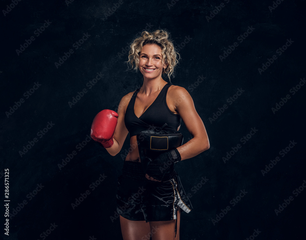 Happy smiling female boxer is posing for photographer at dark photo studio.