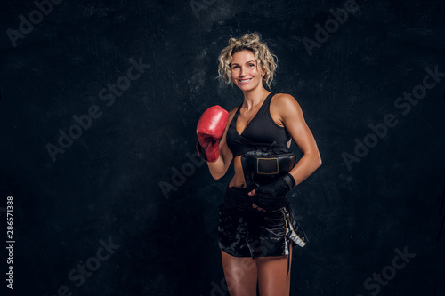 Happy smiling female boxer is posing for photographer at dark photo studio. © Fxquadro