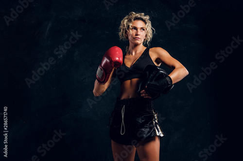 Portrait of powerful strong female boxer in red gloves over dark background. © Fxquadro