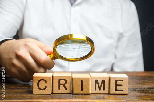 Man with a magnifying glass examines the word Crime. Investigation. Collection evidence, identification of perpetrators, familiarization with court case. Detective, criminal forensic expert. Expertise photo