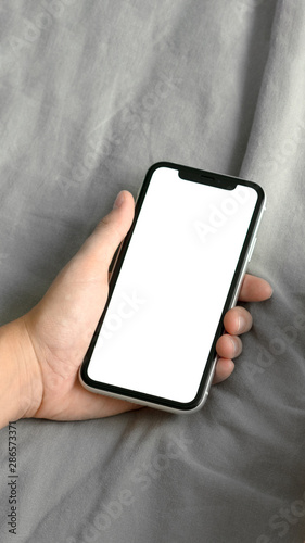 Cropped shot view of woman hands holding smart phone with blank copy space screen for your text message or information content, female reading text message on cell telephone sitting in bed