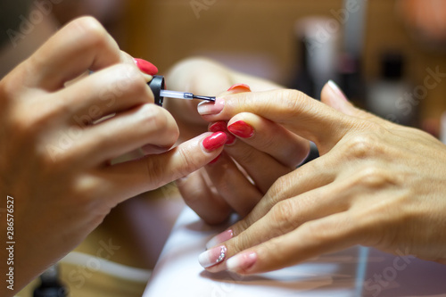 Close up view of female nail painting. Manicurist applying transparent varnish on forefinger nail during final step of her work.