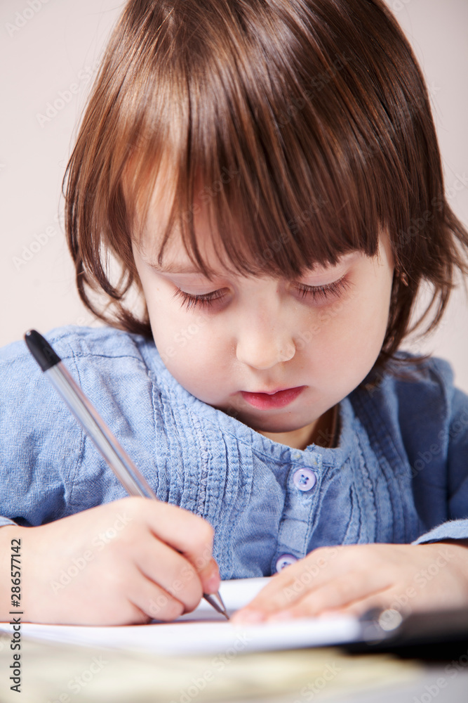 Little cute child girl learning and writing in a workbook. Concept of difficult path to success and victory in the future. Little cute child girl learning and writing in a workbook. Concept of difficult path to success and victory in the future.