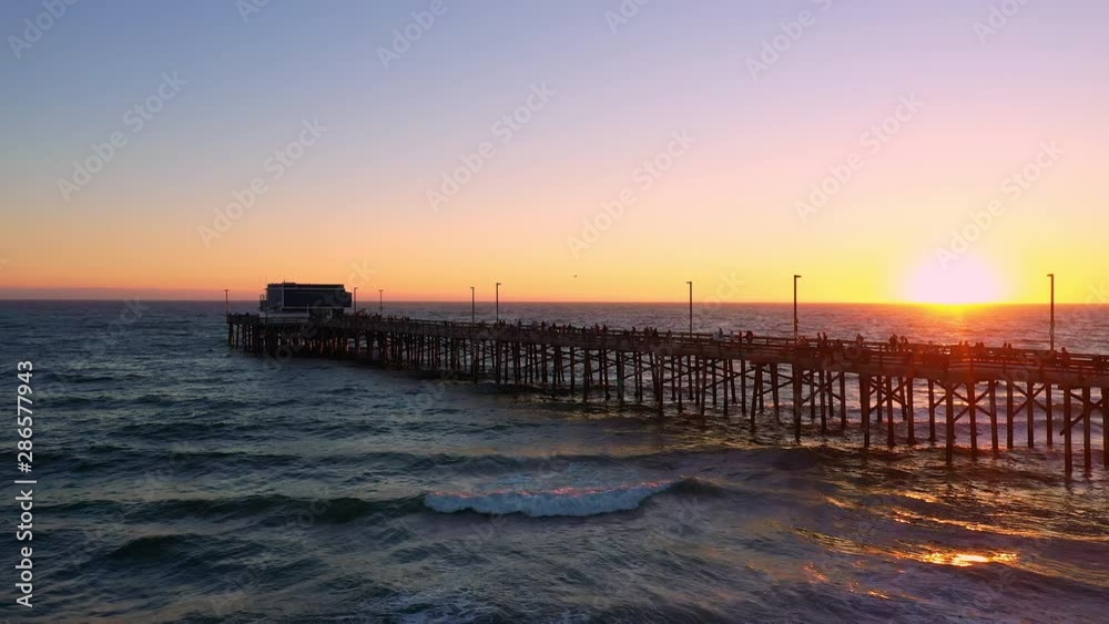Wide aerial view of the Newport Beach pier at sunset moving backwards over the beach. Wide aerial view of the Newport Beach pier at sunset moving backwards over the beach.
