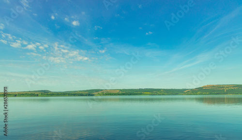 colorful and peaceful nature reserve scenery landscape photography of lake water smooth surface horizon green hill of main land and vivid blue sky background 