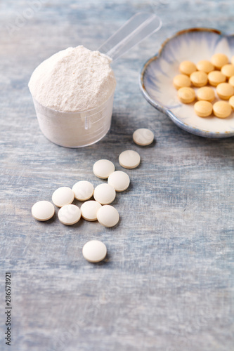 Collagen powder, Hyaluronic Acid and Vitamin C tablets. Supplements to support collagen production. Bright wooden background. Close up. Copy space.