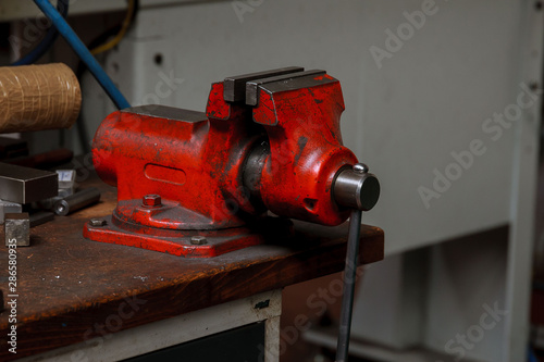 Red Metal vice on wooden table on factory