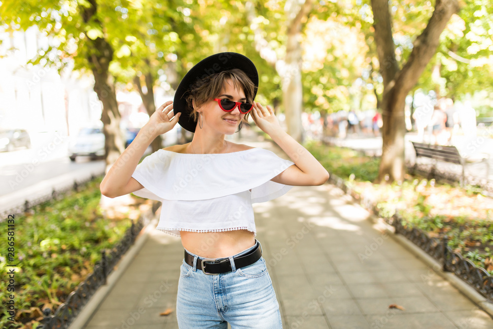 Beautiful young woman in hat and sunglasses walking in the city. Beautiful young woman in hat and sunglasses walking in the city.