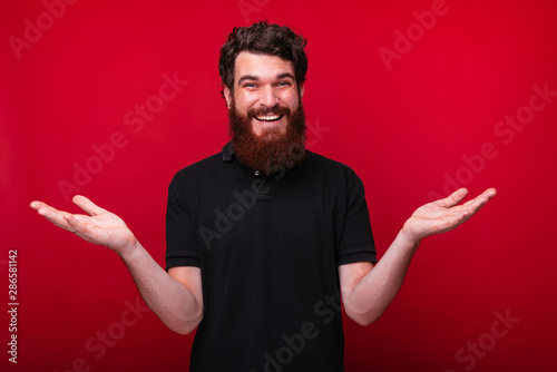 Bearded man is making I don't know or whatever gesture lifting both hands on red background. photo