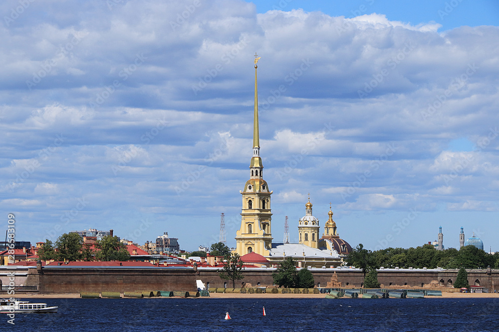 Russia, Petersburg, June 29, 2019. Spit of Vasilyevsky Island. The photo shows the Peter and Paul Fortress on the bank of the Neva against the sky and a pleasure boat