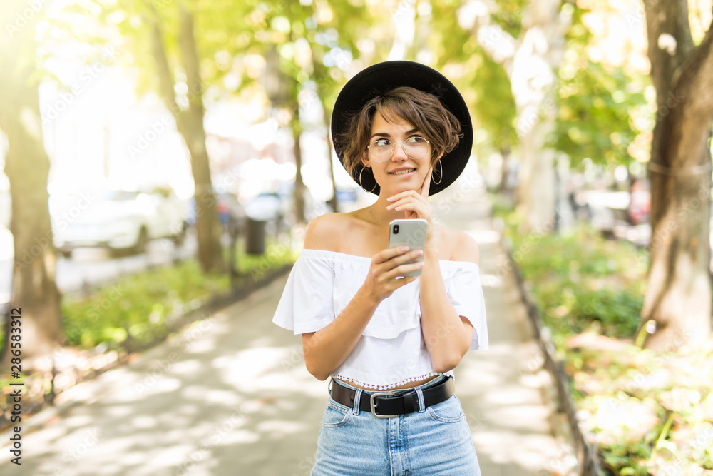 Happy young woman wearing in hat reading good news from her mobile phone. Urban scene. Happy young woman wearing in hat reading good news from her mobile phone. Urban scene.