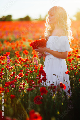 cheerful girl with curly blond hair in a huge poppy field alone, springtime, sunset © Margo Basarab