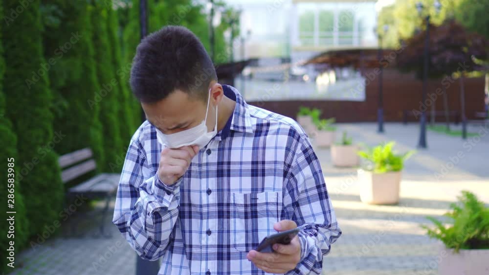 Young asian man with a medical mask on the face coughing and he uses a smartphone Young asian man with a medical mask on the face coughing and he uses a smartphone