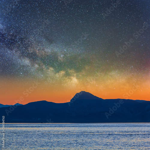 sea bay with rocky coast silhouette under a starry sky, twilight scene