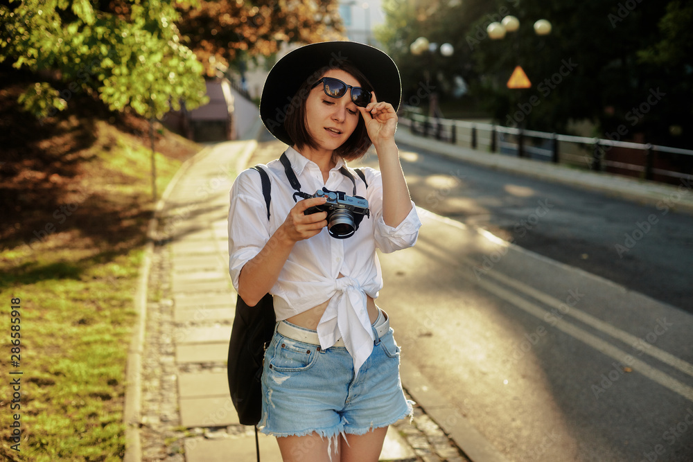 The girl in the black hat and sun glasses with photo camera on a road in an old european town. The girl in the black hat and sun glasses with photo camera on a road in an old european town.