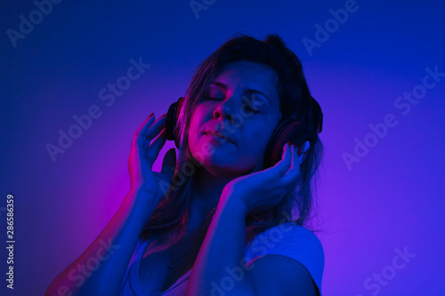 Neon light portrait of happy pretty woman with headphones listening to music