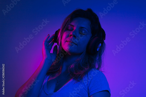 Neon light portrait of happy pretty woman with headphones listening to music