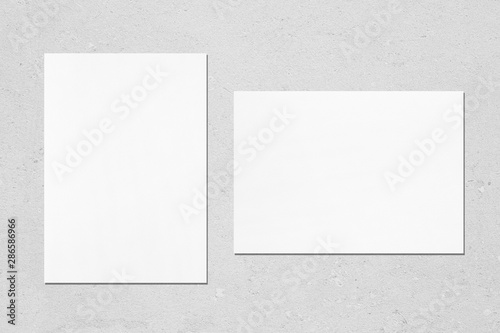 Two empty white vertical and horizontal rectangle poster mockups with soft shadows on neutral light grey concrete background. Flat lay, top view © Aleksandra Konoplya