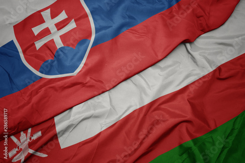 Photography waving colorful flag of oman and national flag of slovakia.