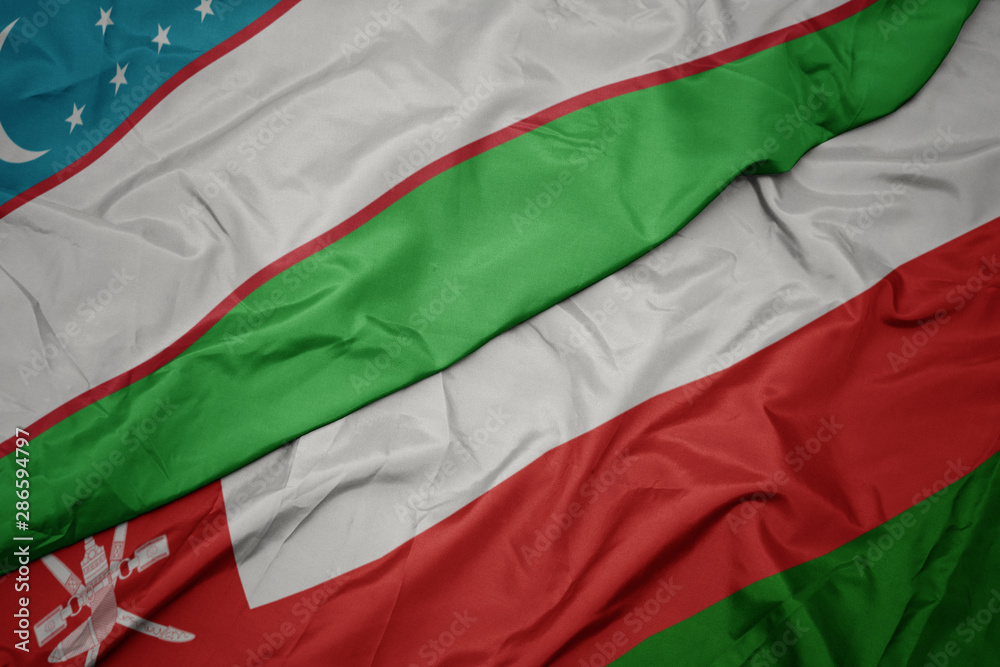 waving colorful flag of oman and national flag of uzbekistan.