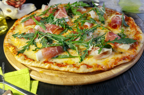 Pizza with bacon, cheese and herbs on a wooden dish on a black wooden background