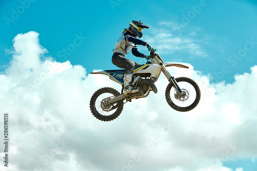 Racer on motorcycle dirtbike motocross cross-country in flight, jumps and takes off on springboard against sky. Concept active extreme rest. © Georgii