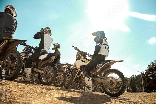 Fototapeta Naklejka Na Ścianę i Meble -  Several extreme motorcyclists are preparing for off-road driving, rear view against a blue sky. Extreme concept, moto races.
