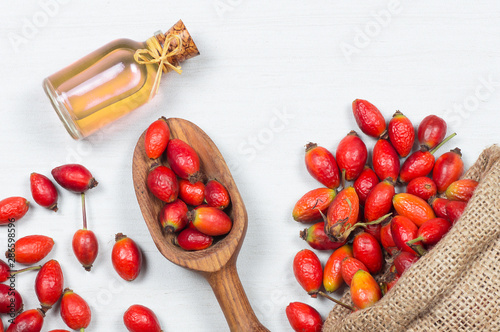 Photography Glass bottle of rosehip seed essential oil with fresh rose hip fruits on white rustic background