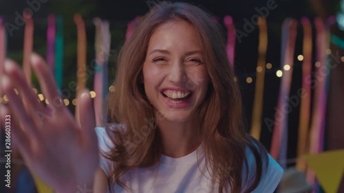 Portrait of pretty playful girl looking serious then bursting into laughter hanging out at the party with friends on decorated cafe terrace at night.