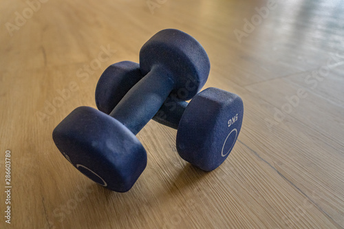 Two crossed lilac dumbbells with five kilogram weight on wooden floor. High angle view, close-up.