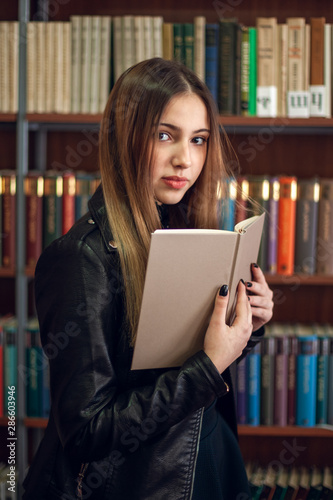 Beautiful teenager schoolgirl reading a book in the library