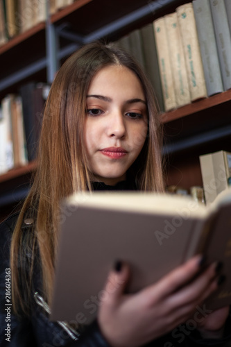 Beautiful teenager schoolgirl reading a book in the library