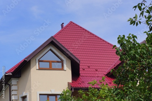 attic of a house with a window and a red tiled roof against a blue sky