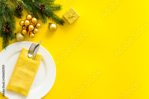 Table setting with spruce, plate, flatware on yellow background top view mockup photo