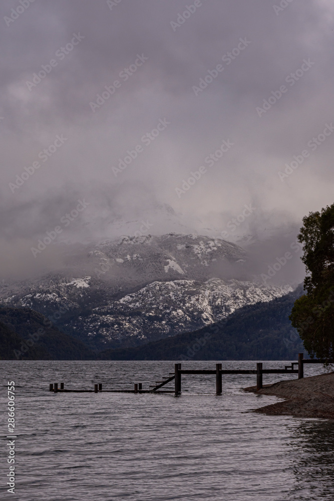 Scene view of wooden pier against snow-capped Andes mountains on a gray day in Los Alerces National Park, Patagonia, Argentina