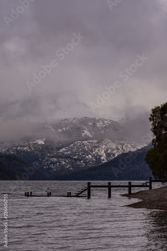 Scene view of wooden pier against snow-capped Andes mountains on a gray day in Los Alerces National Park, Patagonia, Argentina