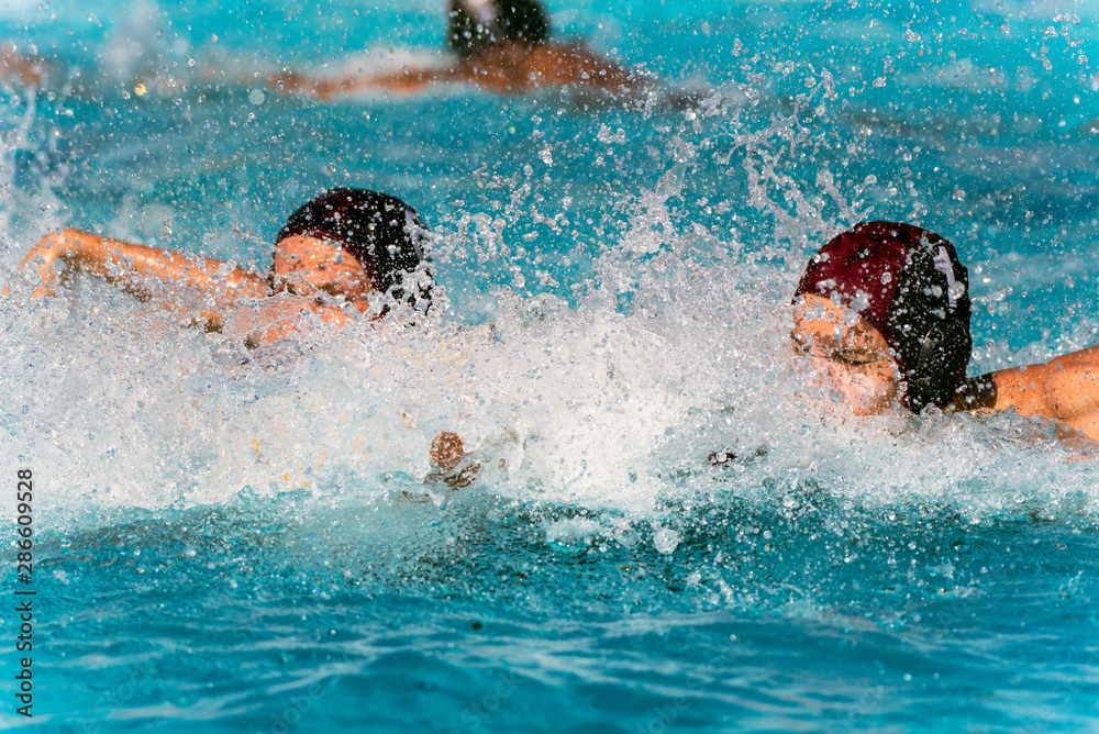 Water Polo team mates in black uniform covered by splashed water drops while racing to the defensive side of pool.