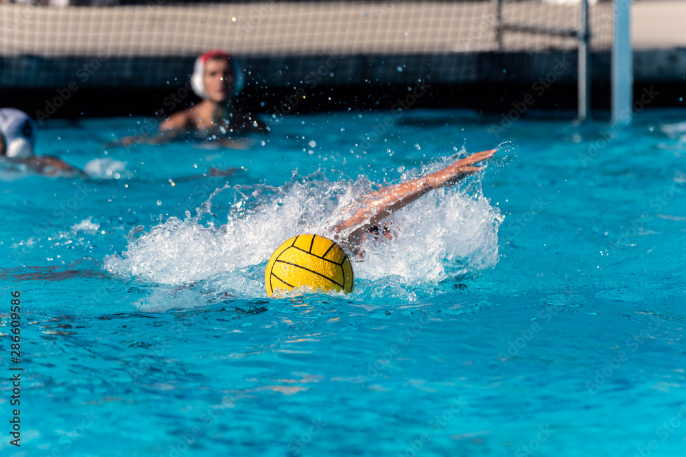 Floating water polo ball and emerging arm from submerged player while goalie looks on during competition match.