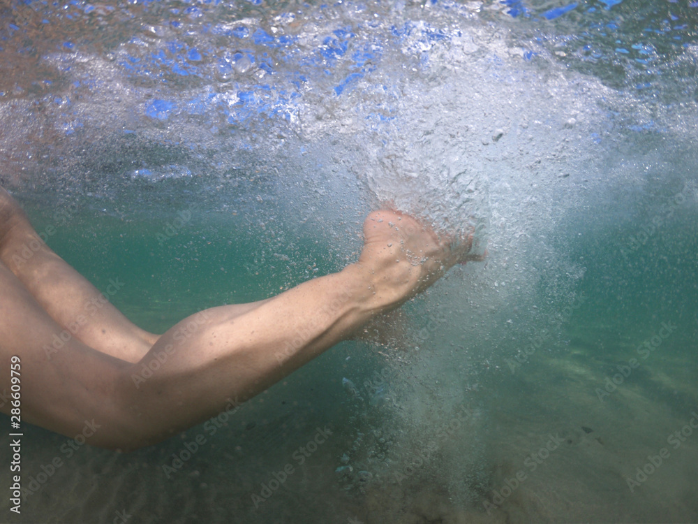Fototapeta premium Unidentified woman's feet underwater swimming with effort and releasing air bubbles to reach the shore