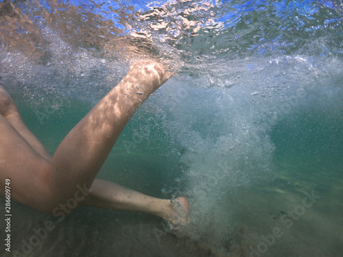 Unidentified woman's feet underwater swimming with effort and releasing air bubbles to reach the shore