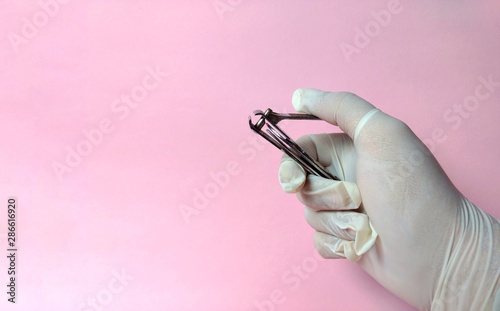Hand with white glove with a nail clipper to care for a patient on pink background. medical concept