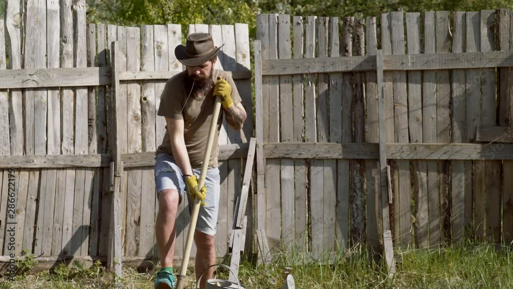 Bearded farmer with shovel. Man hold shovel. Western cowboy wearing cowboy hat - close up portrait. Earth day. Eco living. Emotional funny bearded hipster on the farm on wooden background. Bearded farmer with shovel. Man hold shovel. Western cowboy wearing cowboy hat - close up portrait. Earth day. Eco living. Emotional funny bearded hipster on the farm on wooden background.