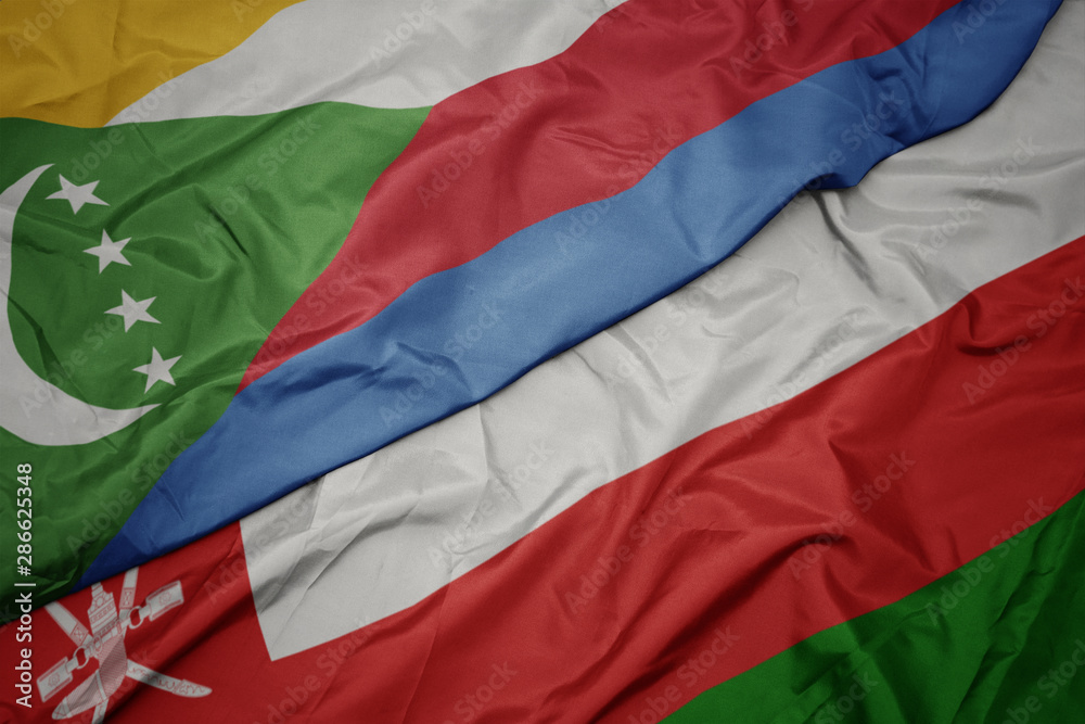 waving colorful flag of oman and national flag of comoros.