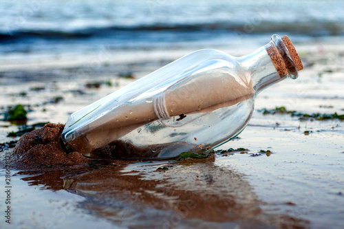 Obraz na płótnie Asking for assistance, optimism and survivor desperation to contact the world conceptual idea with a message in a glass bottle with a cork washing away on sandy beach with the ocean in the background w salonie