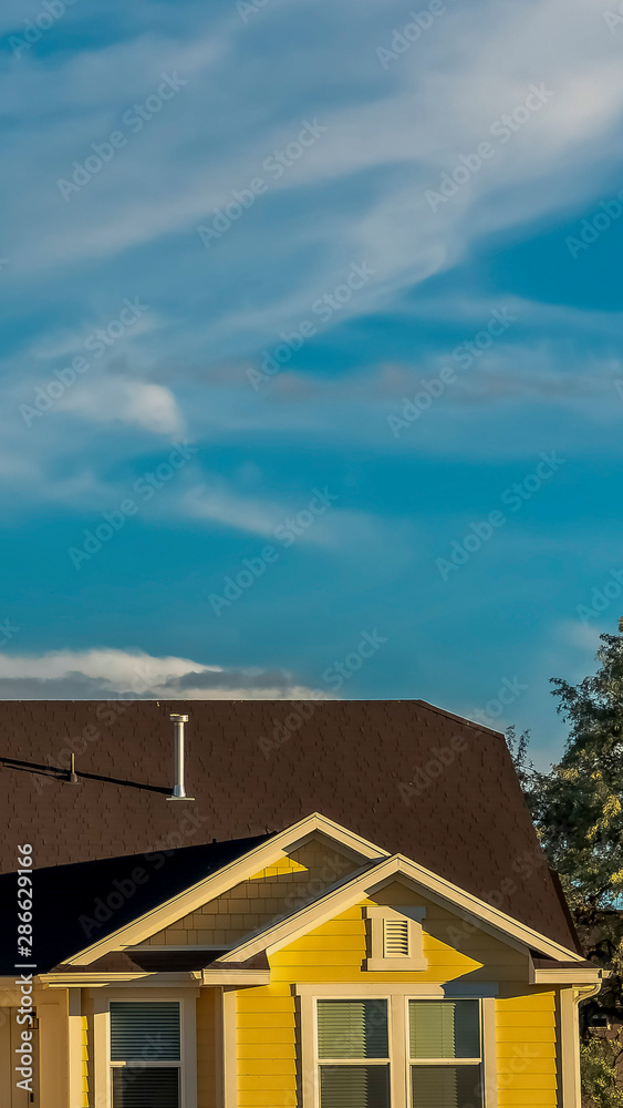 Vertical Home exterior with dark roof and cream wall viewed against sunny cloudy blue sky
