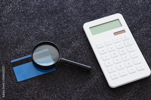 payment card and magnifying glass analyzing it with calculator