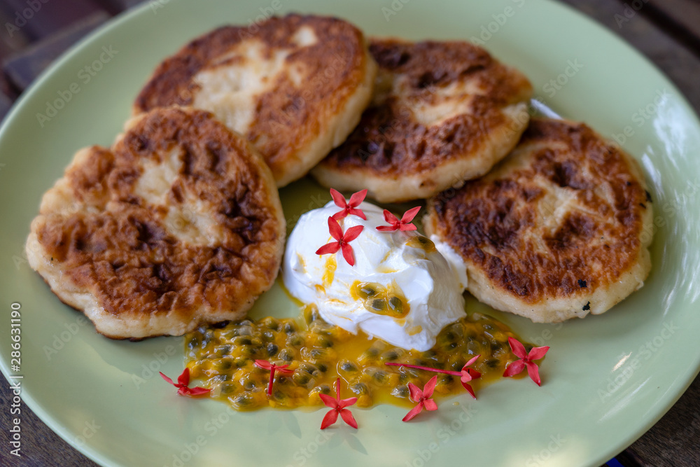 Cheesecakes with passion fruit and sour cream in a green plate for breakfast. Delicious dessert, closeup Cheesecakes with passion fruit and sour cream in a green plate for breakfast. Delicious dessert, closeup